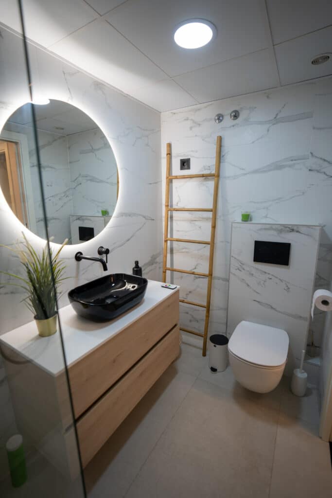 Baño moderno con lavabo negro y mueble volado, espejo con LED redondo