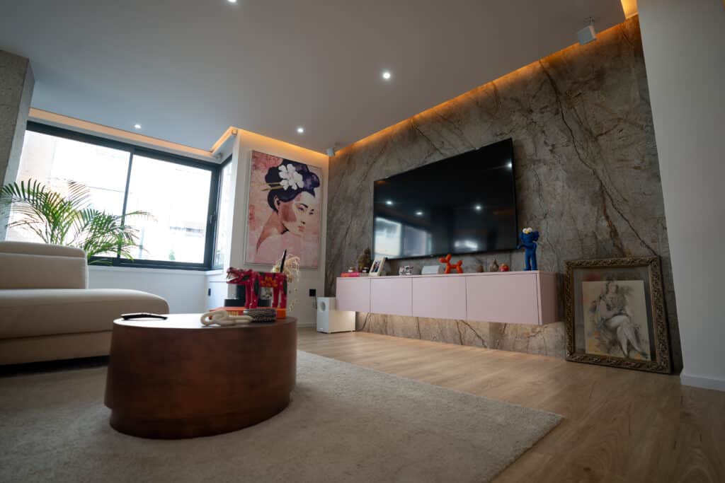 Salón con pared efecto piedra, televisión grande en pared, mueble volado, cuadro de geisha, planta de interior y mesa de centro