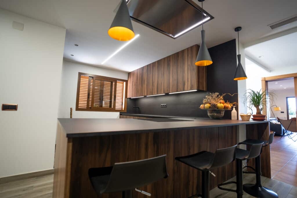 Cocina de madera oscura con lámparas colgantes metálicas oscuras y doradas con taburetes altos