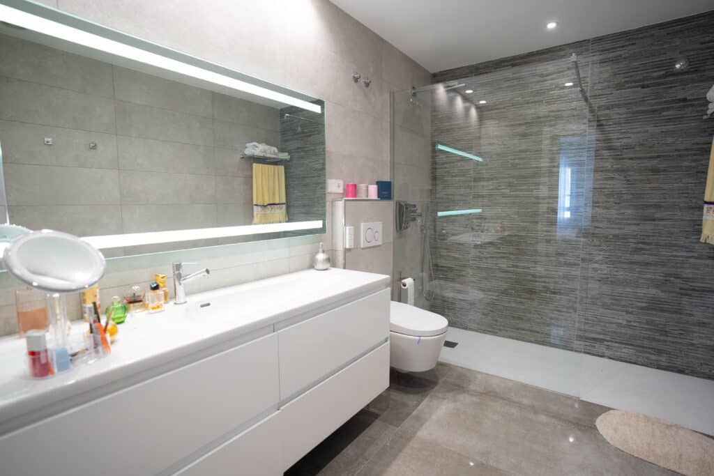 Baño con lavabo largo y espejo gigante con ducha grande y mampara de cristal