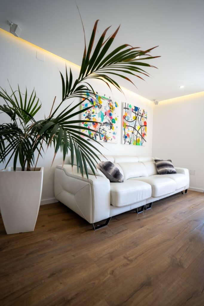 Salón con sofá blanco tapizado y gran palmera de interior